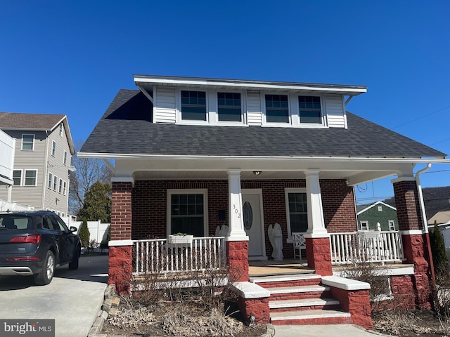 bungalow featuring brick siding, covered porch, and roof with shingles