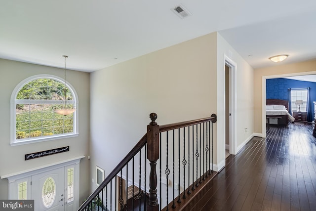 hallway featuring visible vents, baseboards, dark wood-type flooring, and an upstairs landing