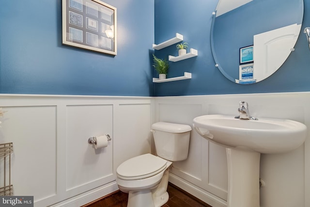 half bathroom featuring wood finished floors, wainscoting, a decorative wall, and toilet