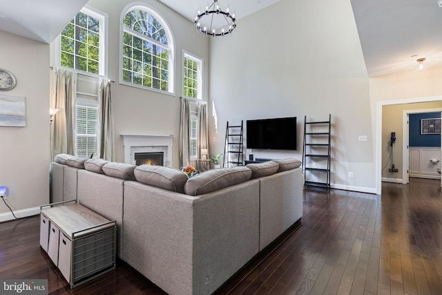 living area featuring a towering ceiling, baseboards, a high end fireplace, a chandelier, and dark wood finished floors