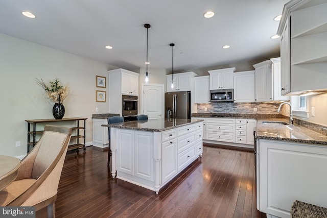 kitchen featuring appliances with stainless steel finishes, tasteful backsplash, a center island, open shelves, and a sink