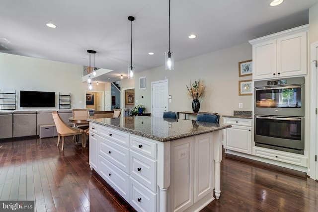 kitchen with a center island, double oven, dark stone countertops, and dark wood-type flooring