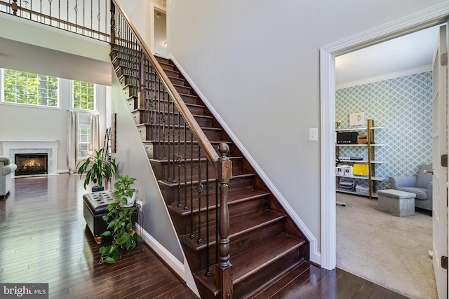 stairway featuring wood-type flooring, ornamental molding, an accent wall, baseboards, and wallpapered walls