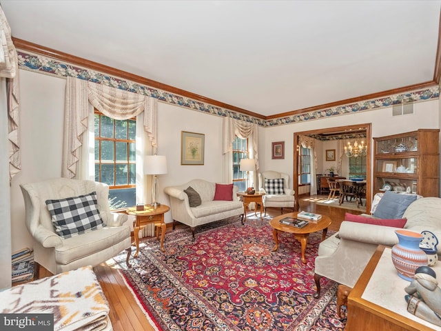 living area featuring hardwood / wood-style floors, visible vents, ornamental molding, and a chandelier