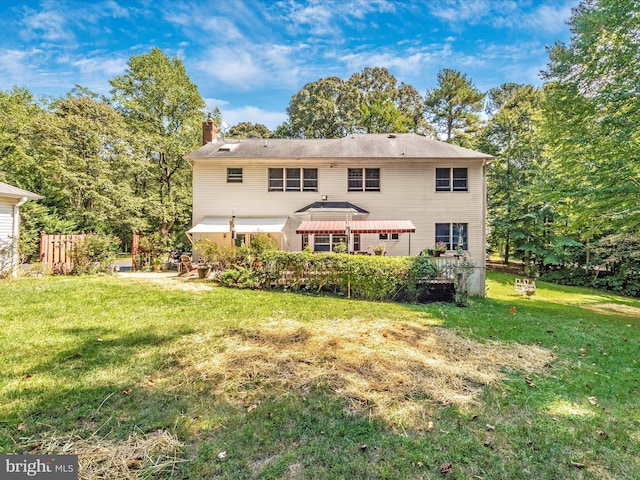 back of house featuring a lawn, a chimney, and fence