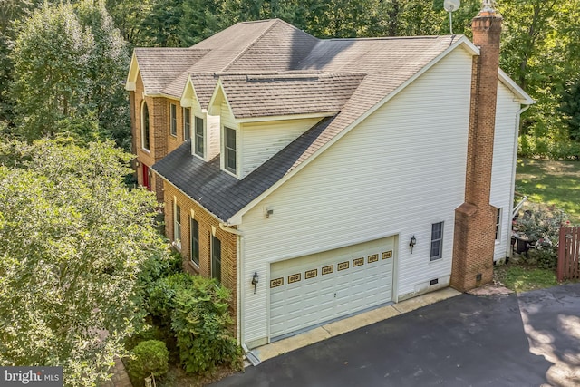 view of side of property with a chimney, roof with shingles, and aphalt driveway
