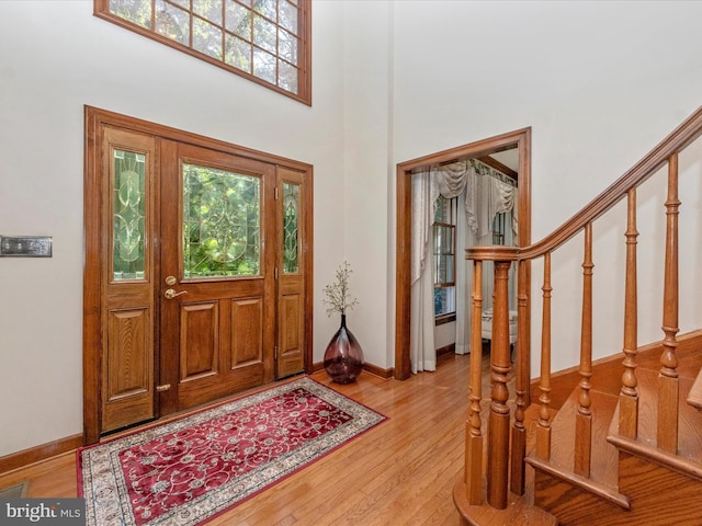 foyer featuring a high ceiling, light wood-style flooring, baseboards, and stairway