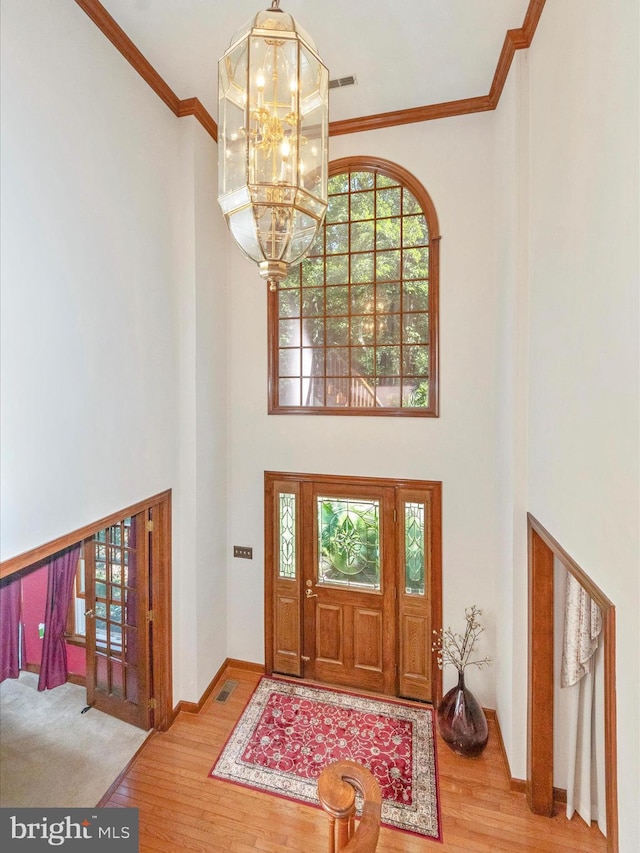 foyer with an inviting chandelier, ornamental molding, a towering ceiling, visible vents, and wood finished floors