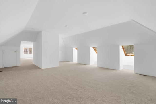 additional living space with visible vents, vaulted ceiling, and light carpet