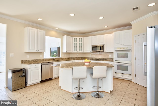 kitchen with appliances with stainless steel finishes, a sink, a center island, white cabinetry, and light tile patterned floors
