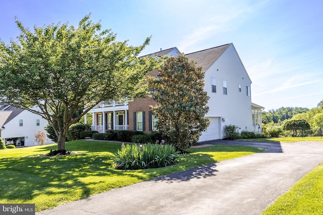 view of property hidden behind natural elements featuring an attached garage, asphalt driveway, a front yard, and brick siding