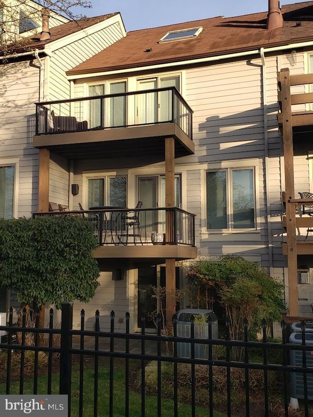 rear view of house featuring central air condition unit, fence private yard, and a balcony