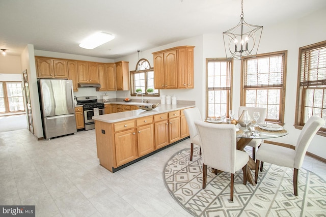 kitchen featuring a peninsula, under cabinet range hood, appliances with stainless steel finishes, light countertops, and a notable chandelier