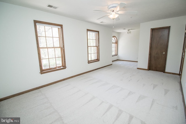 spare room featuring visible vents, light colored carpet, a ceiling fan, and plenty of natural light