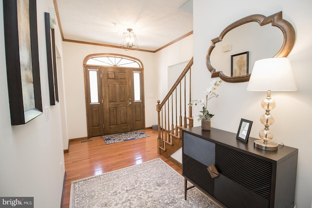 foyer with wood finished floors, an inviting chandelier, ornamental molding, and stairs