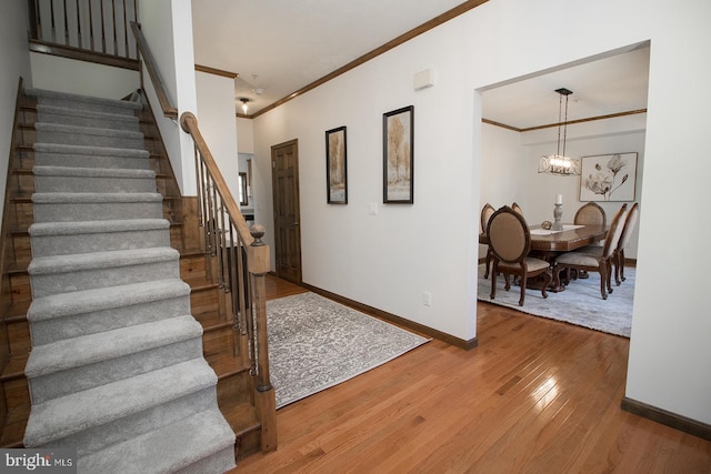 entryway featuring baseboards, a chandelier, crown molding, stairs, and wood-type flooring