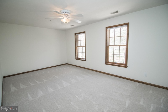 spare room featuring visible vents, light colored carpet, baseboards, and ceiling fan