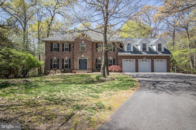 colonial inspired home with brick siding, a front yard, a garage, and driveway
