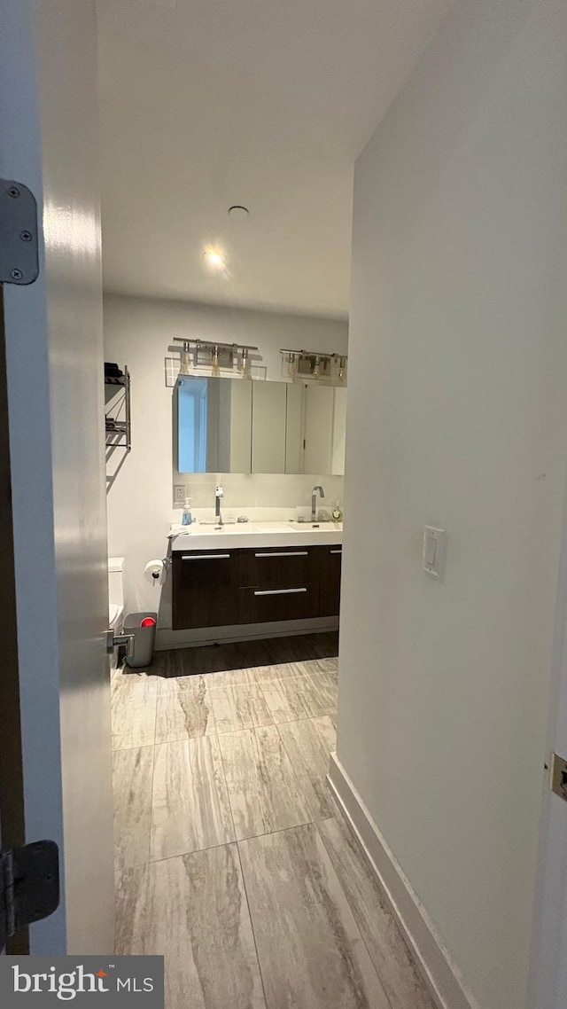 full bath featuring a sink, double vanity, wood finished floors, and baseboards