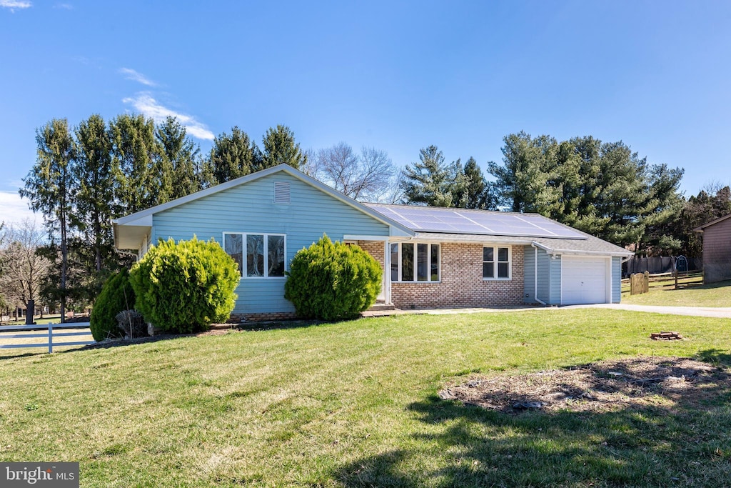 ranch-style home featuring roof mounted solar panels, a garage, fence, brick siding, and concrete driveway