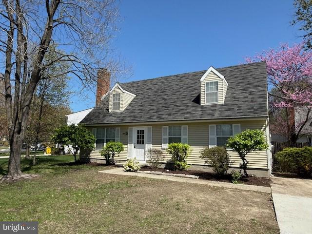 cape cod-style house with a chimney and a front yard