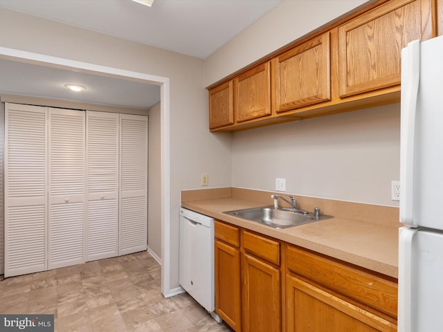 kitchen featuring a sink, brown cabinets, white appliances, light countertops, and baseboards