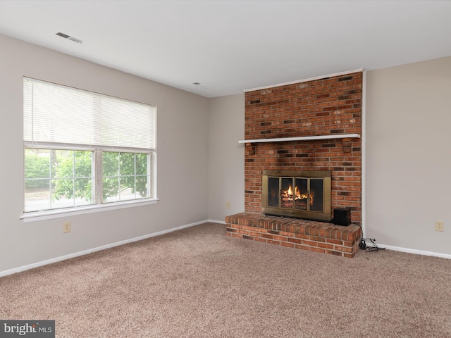 unfurnished living room with a brick fireplace, baseboards, carpet flooring, and visible vents
