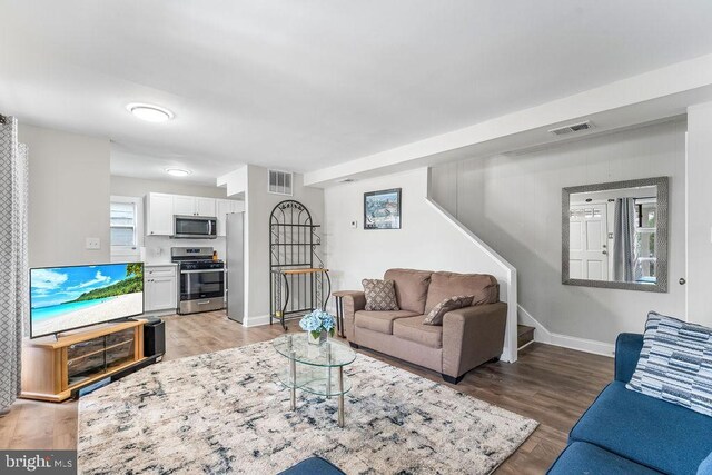 living area featuring visible vents, baseboards, light wood-style floors, and stairs