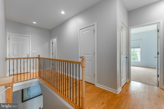 hall featuring light wood-style flooring, an upstairs landing, baseboards, and recessed lighting