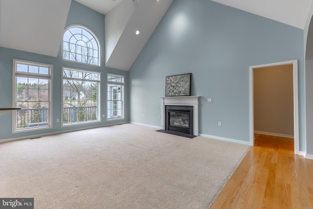 unfurnished living room with baseboards, high vaulted ceiling, a fireplace with flush hearth, and carpet