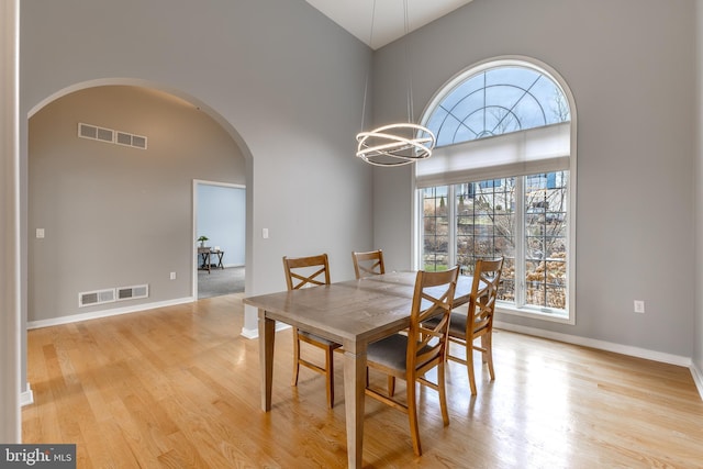 dining space featuring high vaulted ceiling, arched walkways, visible vents, a notable chandelier, and wood finished floors