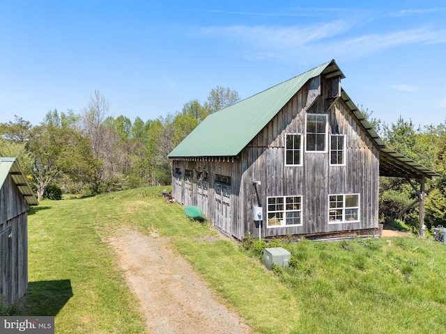 view of side of property with an outdoor structure, a garage, metal roof, a lawn, and driveway