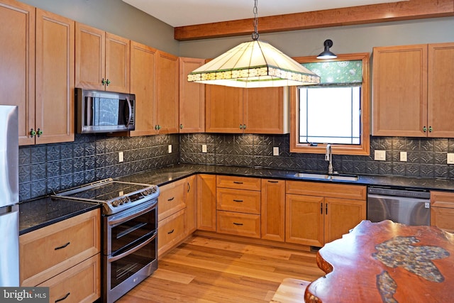 kitchen with decorative light fixtures, light wood-type flooring, backsplash, a sink, and appliances with stainless steel finishes