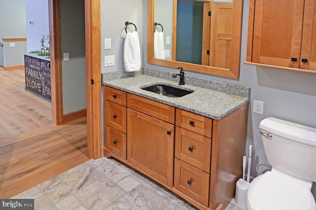 bathroom with baseboards, wood finished floors, toilet, and vanity