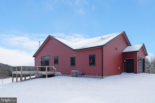 snow covered house featuring central air condition unit, a wooden deck, and a garage