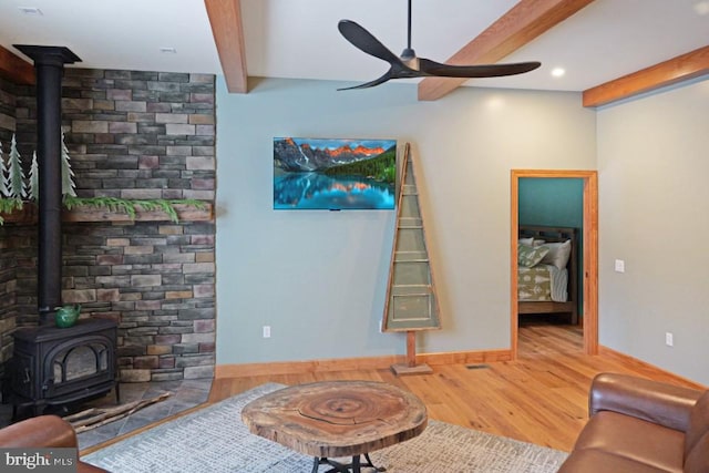 living area with a wood stove, baseboards, beam ceiling, ceiling fan, and wood finished floors