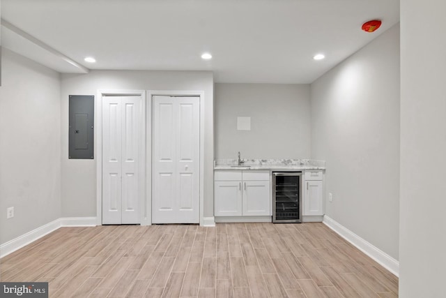 bar featuring electric panel, wet bar, a sink, beverage cooler, and light wood-style floors