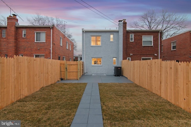 back of house at dusk with a patio area, a chimney, a fenced backyard, central AC unit, and a lawn