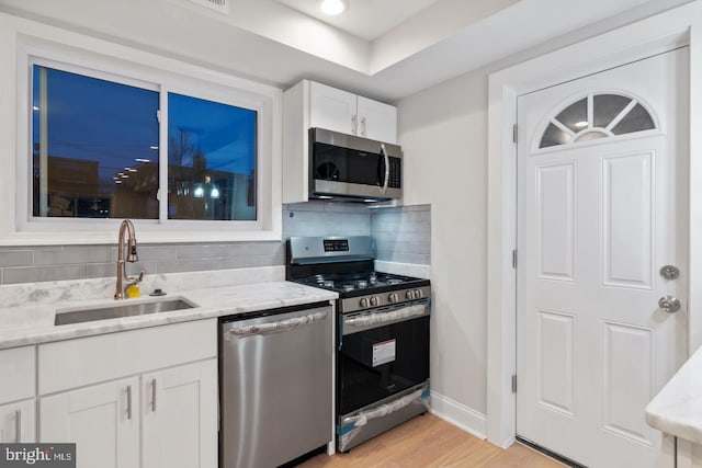 kitchen featuring white cabinets, stainless steel appliances, tasteful backsplash, a sink, and light stone counters