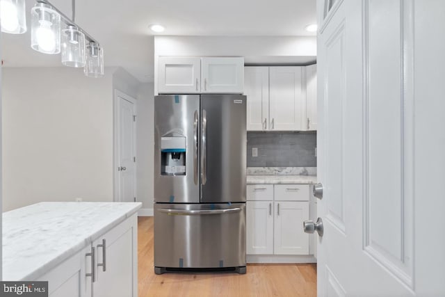 kitchen featuring light wood-style flooring, stainless steel fridge, tasteful backsplash, white cabinetry, and light stone counters