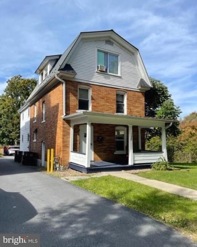 view of front of property with brick siding, a porch, and a gambrel roof