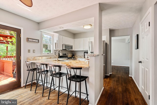 kitchen with stainless steel appliances, a peninsula, dark wood-style flooring, and white cabinetry