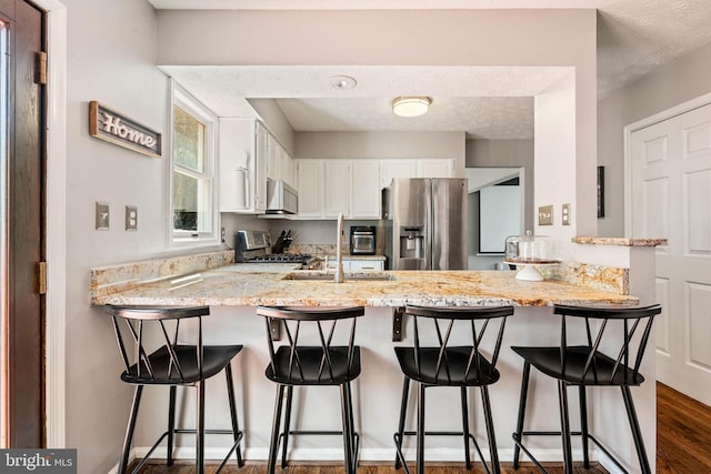 kitchen with dark wood-style flooring, appliances with stainless steel finishes, a peninsula, white cabinetry, and light stone countertops