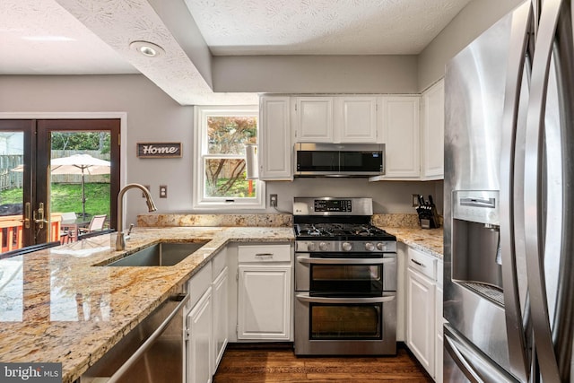 kitchen with light stone counters, a sink, white cabinets, and stainless steel appliances
