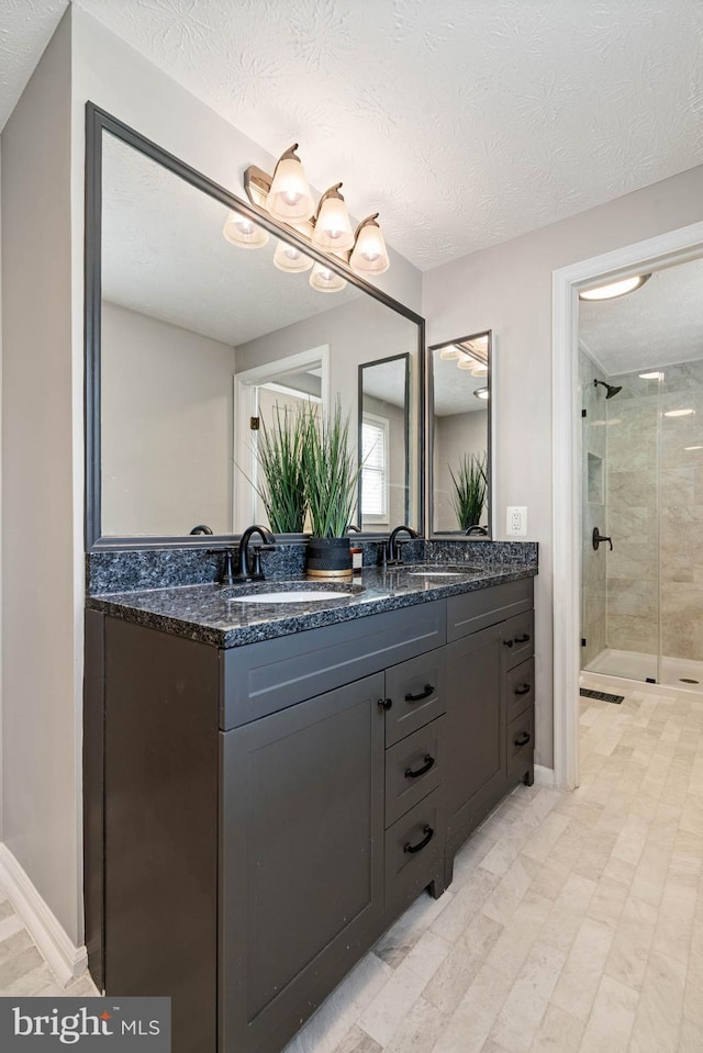 full bath featuring a shower stall, double vanity, a textured ceiling, and a sink