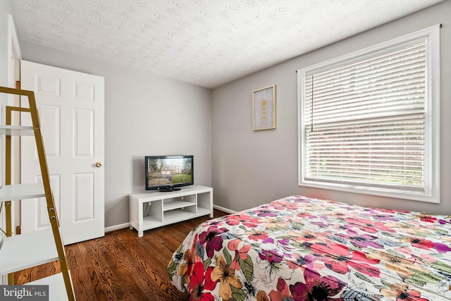 bedroom with baseboards, multiple windows, wood finished floors, and a textured ceiling