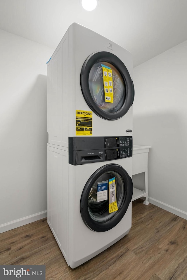 laundry area with laundry area, wood finished floors, stacked washer and clothes dryer, and baseboards