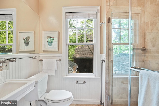 bathroom with toilet, wainscoting, tiled shower, and a decorative wall