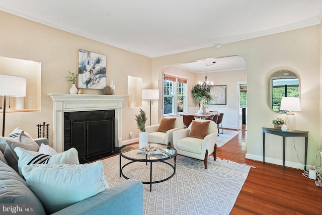 living area with an inviting chandelier, ornamental molding, a fireplace with flush hearth, wood finished floors, and arched walkways