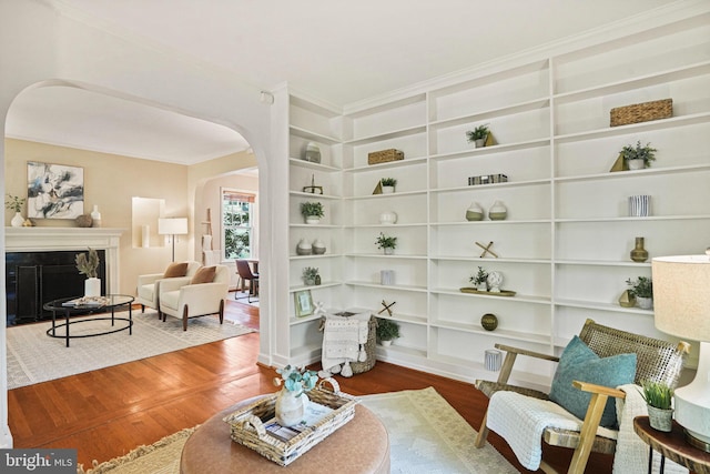 living area with crown molding, arched walkways, built in shelves, and wood finished floors
